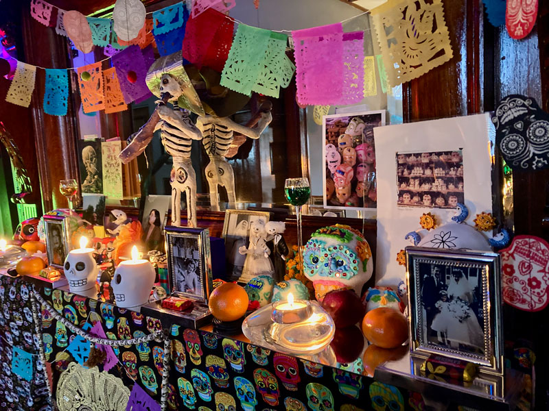 A day of the dead Ofrenda, or memorial altar, with themed art, candles, colorful skulls, photographs, offerings of food and drink