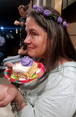 woman wearing purple flower wreath smirking over cake with purple flowers