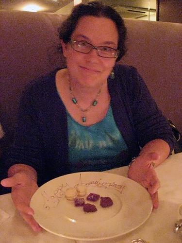 woman smirking at camera, holding plate that says Happy Anniversary