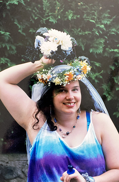 woman wearing tie-dyed dress and flower wreath holding bouquet over her head